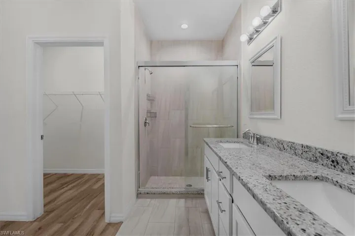 Full bathroom with a walk in closet, double vanity, a shower stall, and light wood-style floors