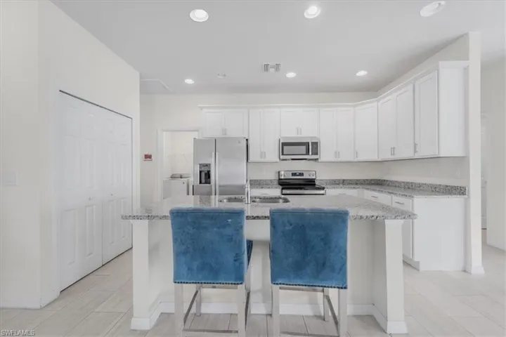 Kitchen featuring light stone counters, stainless steel appliances, white cabinets, a center island with sink, and a kitchen breakfast bar