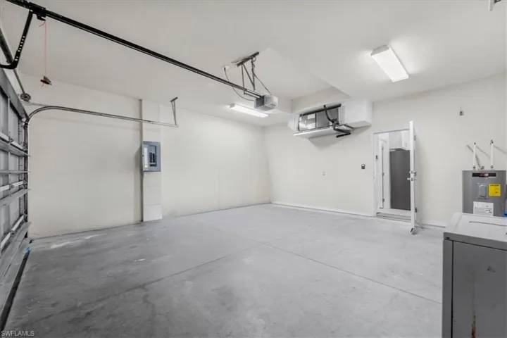 Garage with electric water heater, electric panel, and a garage door opener