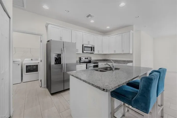 Kitchen featuring white cabinetry, stainless steel appliances, light stone countertops, an island with sink, and a kitchen bar