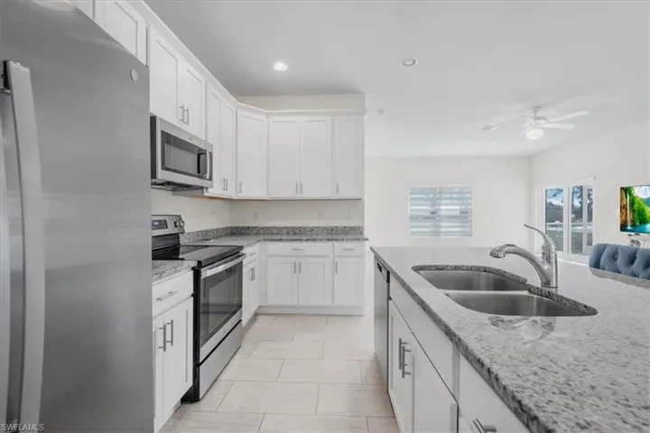 Kitchen featuring stainless steel appliances, light stone countertops, white cabinets, a ceiling fan, and recessed lighting