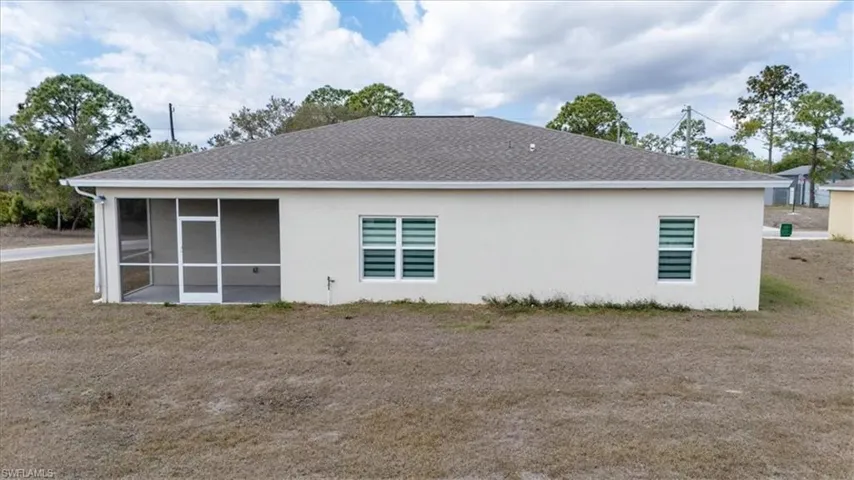 Rear view of property with roof with shingles, stucco siding, and a yard