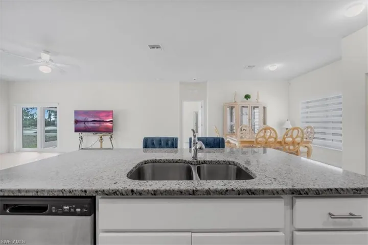 Kitchen with white cabinets, light stone counters, dishwasher, open floor plan, and an island with sink
