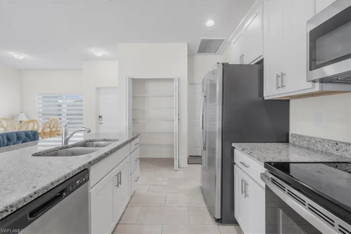 Kitchen with light stone counters, stainless steel appliances, white cabinetry, recessed lighting, and light tile patterned floors