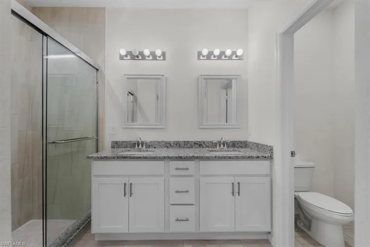 Full bath with double vanity, a shower stall, and light tile patterned floors