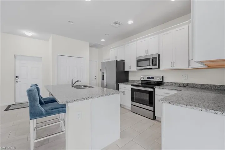 Kitchen featuring stainless steel appliances, a center island with sink, white cabinetry, a breakfast bar area, and light stone countertops