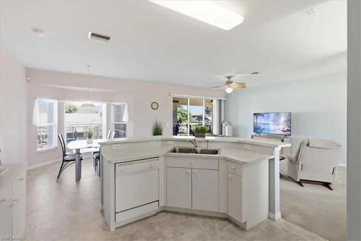 Kitchen featuring a center island with sink, white dishwasher, light countertops, white cabinetry, and decorative light fixtures