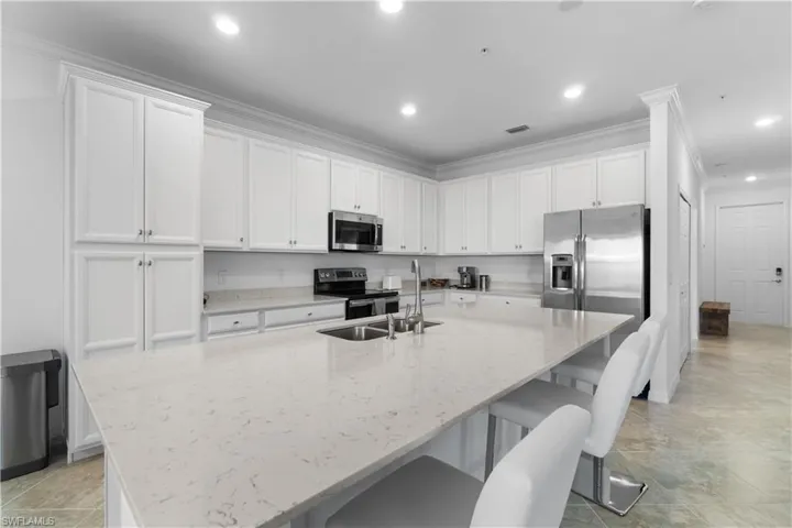 Kitchen featuring white cabinetry, light stone countertops, crown molding, and stainless steel appliances