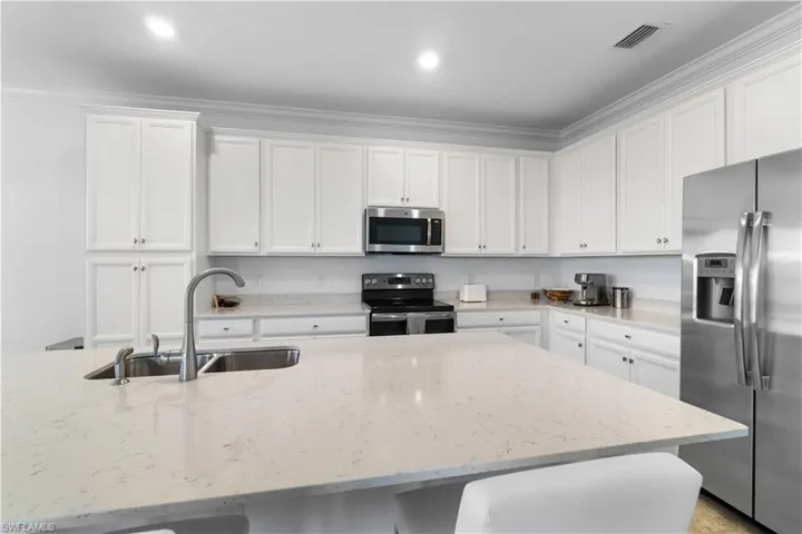 Kitchen featuring sink, light stone counters, stainless steel appliances, and white cabinetry