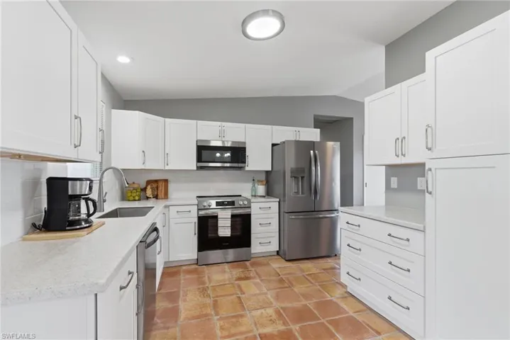 NEW Kitchen with stainless steel appliances, lofted ceiling, white cabinetry, tasteful backsplash, and light stone counters