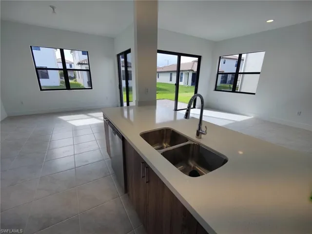 Kitchen with dark brown cabinetry, dishwasher, sink, and light tile patterned floors