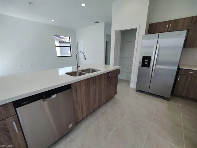 Kitchen featuring sink, light tile patterned floors, stainless steel appliances, and dark brown cabinetry