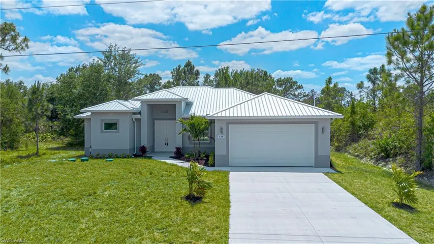 Ranch-style home with a front lawn, stucco siding, metal roof, concrete driveway, and an attached garage