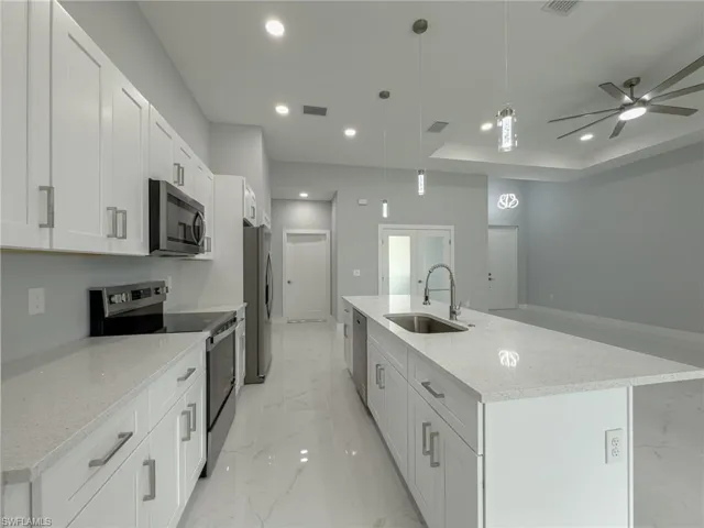 Kitchen featuring a sink, stainless steel appliances, a large island, marble finish floor, and white cabinets