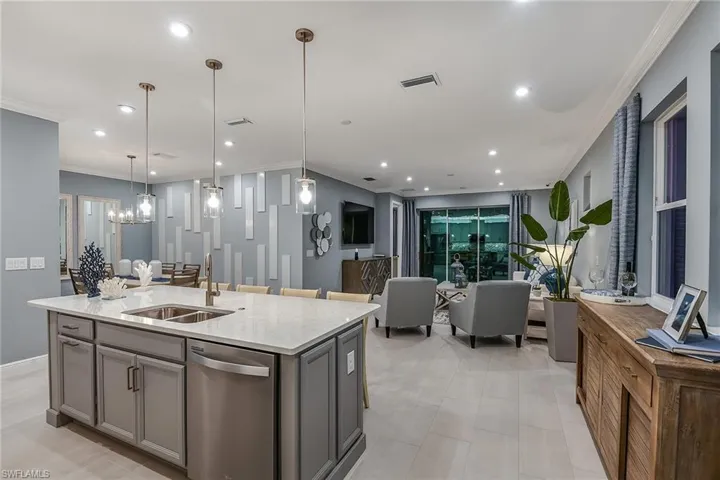 Kitchen with crown molding, light stone countertops, dishwasher, a kitchen island with sink, and pendant lighting