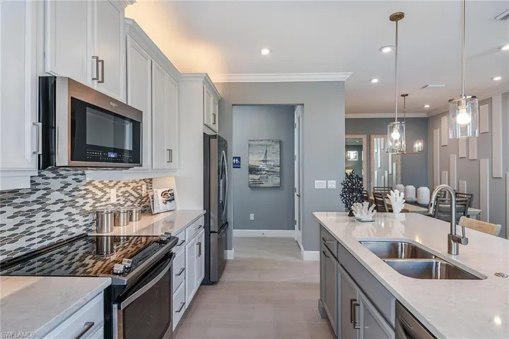 Kitchen featuring stainless steel appliances, light stone counters, gray cabinets, pendant lighting, and crown molding