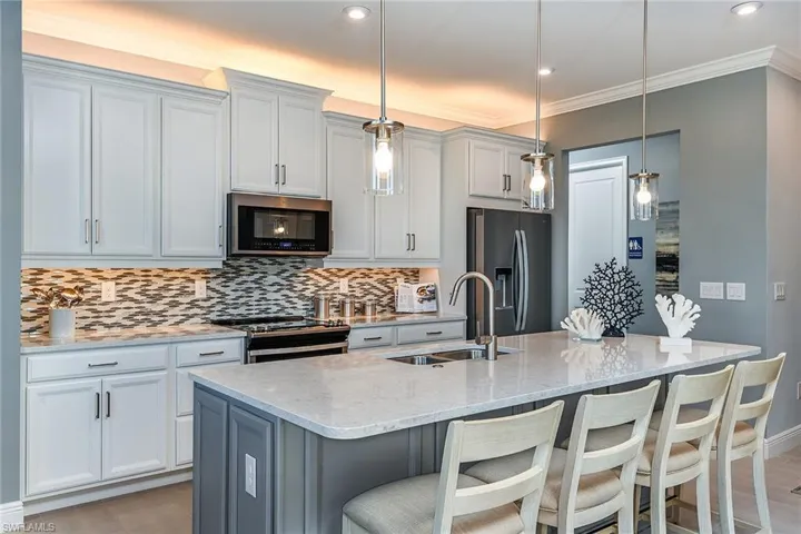 Kitchen with gray cabinetry, light stone counters, stainless steel appliances, a breakfast bar area, and crown molding
