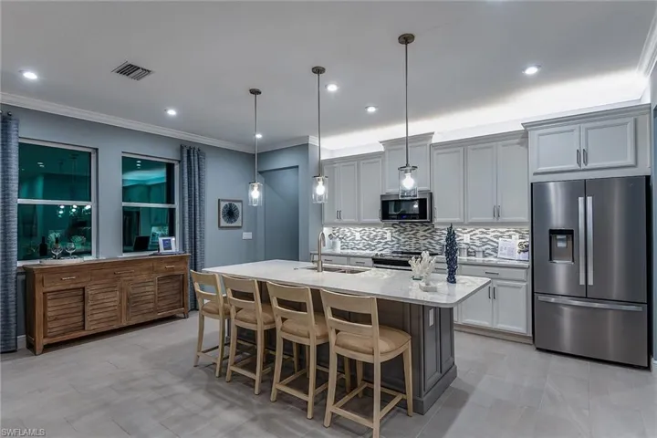Kitchen with stainless steel appliances, a breakfast bar area, light stone counters, decorative backsplash, and decorative light fixtures