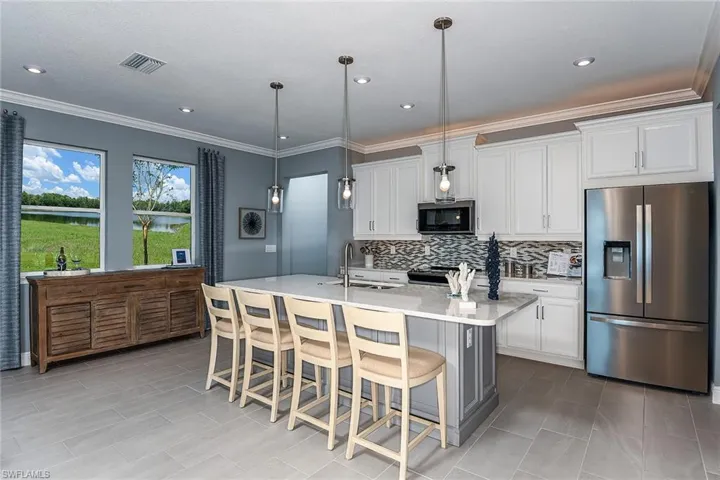 Kitchen with stainless steel appliances, ornamental molding, light stone countertops, a kitchen bar, and white cabinetry