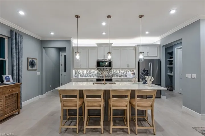 Kitchen with decorative backsplash, stainless steel appliances, light stone counters, a kitchen bar, and ornamental molding