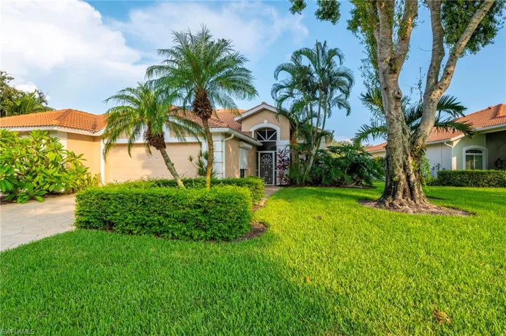 Tan stucco exterior with a terracotta tile roof, arched entryway, decorative security screen door, and mature landscaping