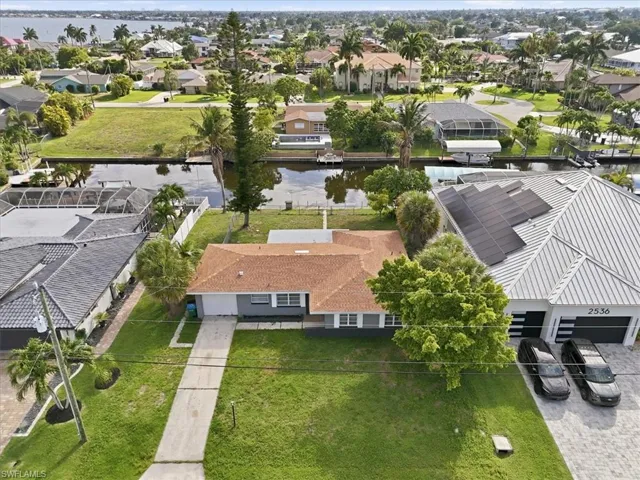 Waterfront property featuring a single-story residence with a terracotta-colored roof and an expansive green lawn