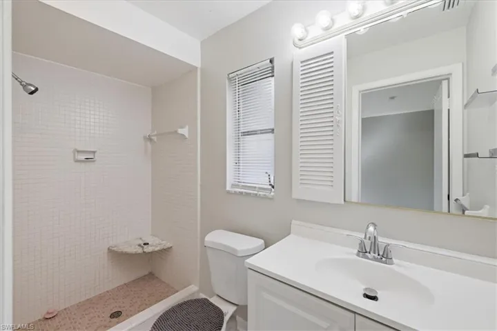 Bathroom featuring a tiled shower with a built-in corner shelf, a single vanity with an integrated sink, a mirrored medicine cabinet with louvered doors, and a window with blinds