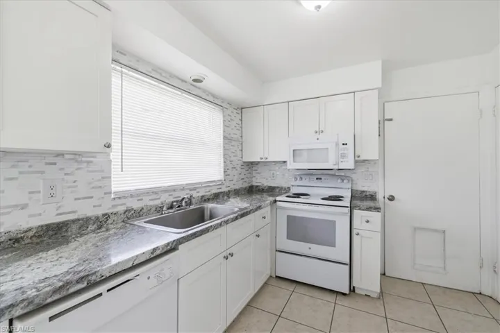 Kitchen featuring white cabinetry, gray patterned countertops, and a white tile backsplash