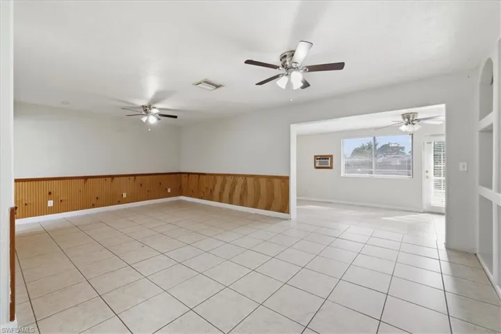 Spacious room with light-toned tile flooring and wood paneling along the lower walls