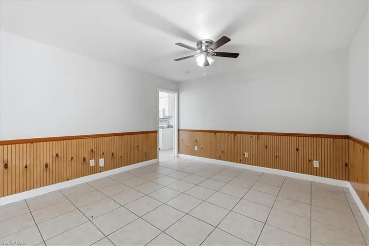 Interior room featuring wood-panel wainscoting, light-toned tile flooring, and a ceiling fan with integrated lighting