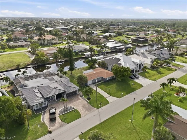 Canal-front property featuring a screened pool enclosure, paved driveway, mature palm trees, and a well-maintained lawn