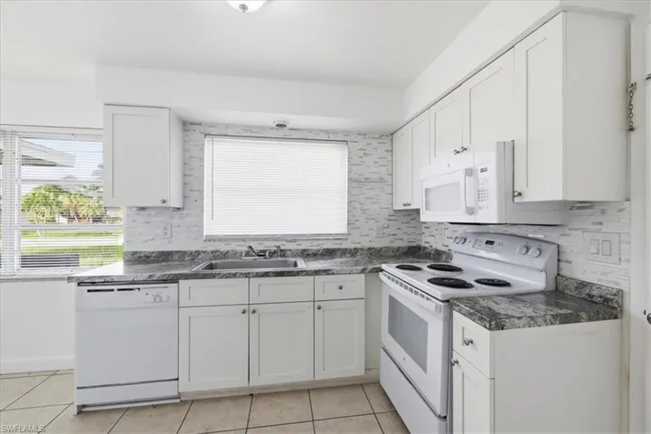 Kitchen featuring white shaker-style cabinetry, granite-finish countertops, and a full suite of appliances
