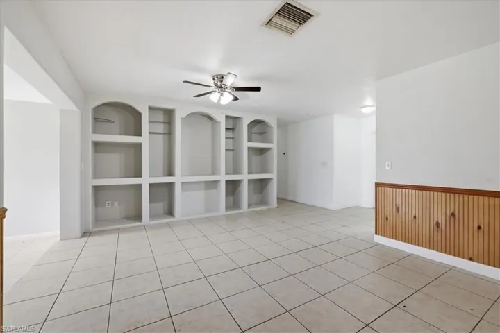 Spacious living area featuring extensive built-in shelving, tile flooring, a ceiling fan, and wood paneling