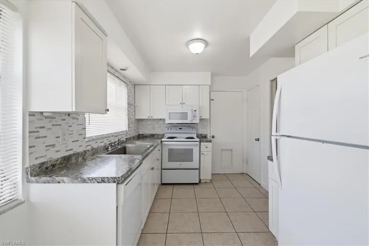 White kitchen with shaker-style cabinetry, a mosaic tile backsplash, and granite-finish countertops