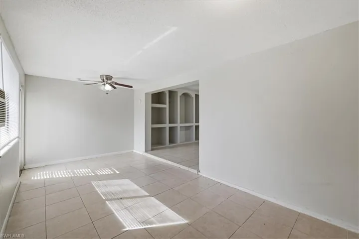 Spacious interior featuring tile flooring, a ceiling fan with integrated lighting, and a built-in shelving unit with arched accents