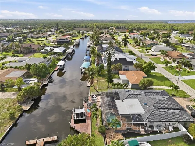 Waterfront property with private dock, screened-in pool enclosure, and mature palm trees