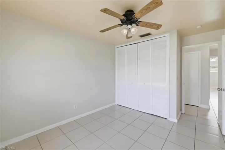 Spacious interior featuring neutral wall paint, tiled flooring, a ceiling fan with light fixture, and a built-in louvered bi-fold closet