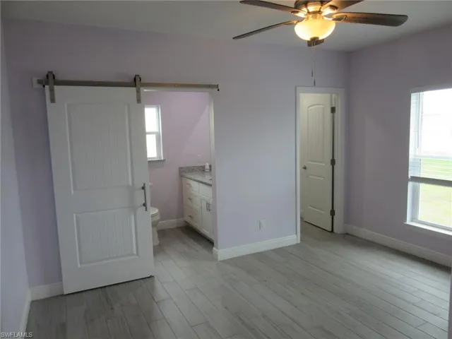 Spare room featuring a barn door, a ceiling fan, light wood finished floors, and plenty of natural light