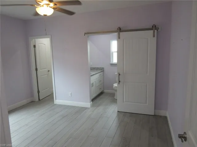 Unfurnished bedroom featuring light wood-style flooring, a barn door, and ceiling fan