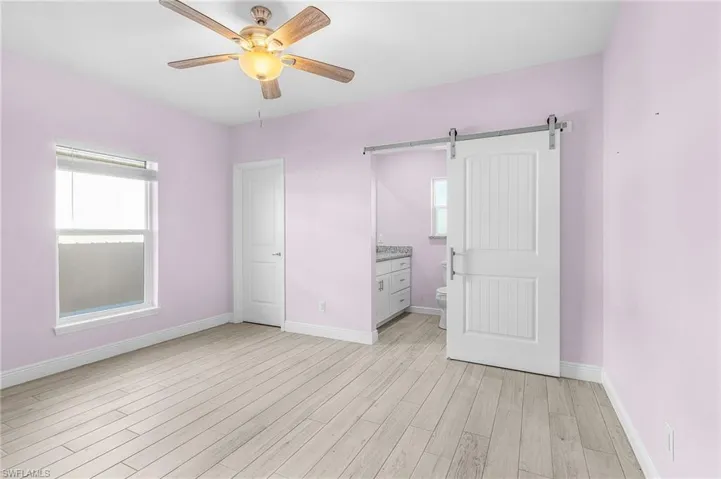 Unfurnished bedroom with a barn door, light wood finished floors, a ceiling fan, and connected bathroom