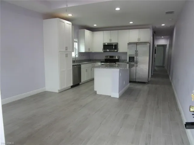 Kitchen with stainless steel appliances, white cabinets, a center island, light wood-style flooring, and recessed lighting