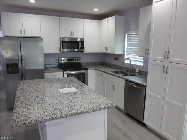 Kitchen featuring appliances with stainless steel finishes, white cabinets, recessed lighting, light stone counters, and a center island