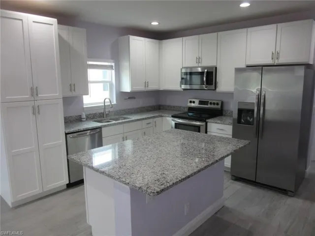 Kitchen featuring appliances with stainless steel finishes, light wood-style flooring, white cabinetry, light stone counters, and recessed lighting