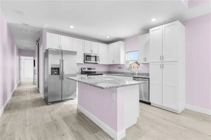 Kitchen featuring appliances with stainless steel finishes, light stone countertops, white cabinets, a kitchen island, and recessed lighting