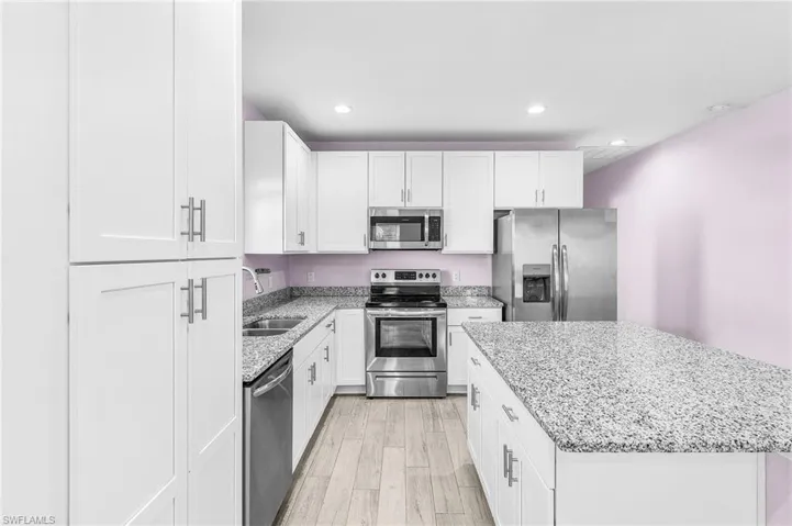 Kitchen with appliances with stainless steel finishes, a kitchen island, light wood-style flooring, light stone counters, and recessed lighting
