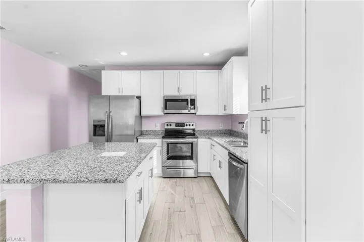 Kitchen with stainless steel appliances, a kitchen island, white cabinets, light wood-style floors, and light stone countertops