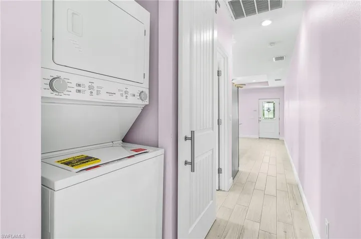 Laundry area featuring stacked washer and clothes dryer, light wood-type flooring, and recessed lighting