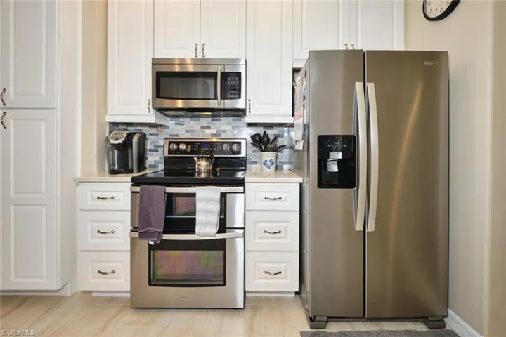 Kitchen with stainless steel appliances, white cabinetry, backsplash, and light stone countertops