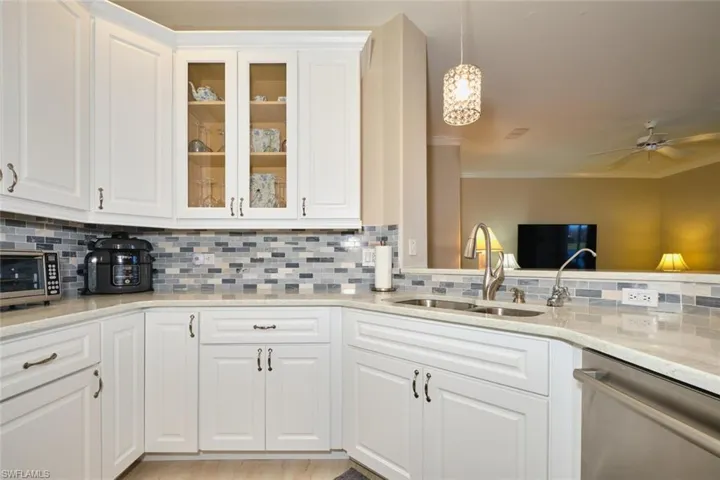 Kitchen with white cabinetry, dishwasher, pendant lighting, light stone countertops, and crown molding
