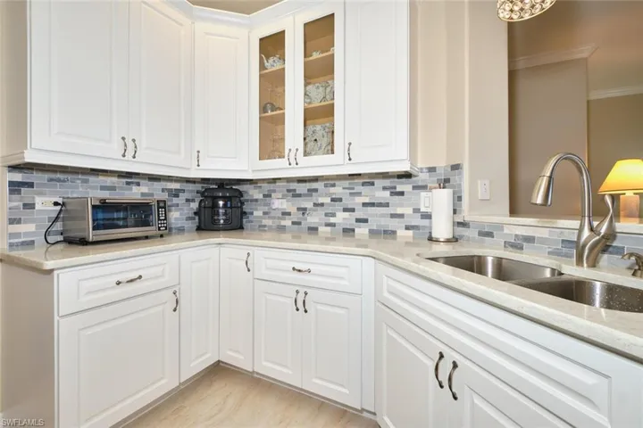 Kitchen with white cabinets, light stone counters, glass fronted cabinets, crown molding, and backsplash